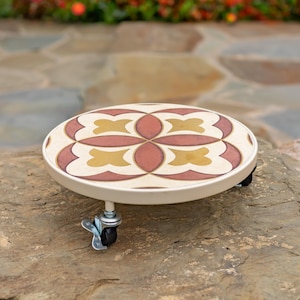 May include: A round, white plant stand with a decorative tile design in shades of brown, red, and gold. The stand has four small wheels for easy movement.