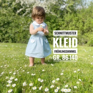 May include: A blue and white patterned dress with a white collar and pockets. The dress is for a child and is shown on a model standing in a field of white flowers. The text on the image reads "Schnittmuster Kleid Frühlingshimmel GR. 86-140".