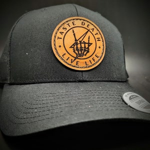 May include: Black trucker hat with a brown leather patch that says "Taste Death Live Life" with a skeleton hand making a rock and roll sign.