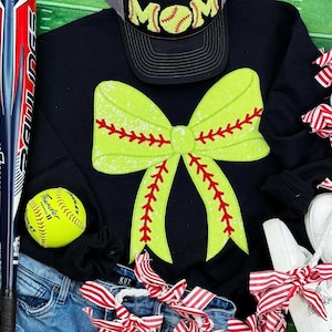 May include: Black sweatshirt with a large green and red bow with a baseball stitch design. The bow is made of sequins. The sweatshirt has the word "MOM" on a black baseball cap.