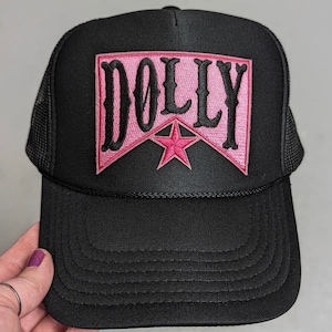 May include: Black trucker hat with a pink patch that says "DOLLY" in black lettering with a red star.