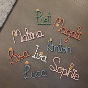 Könnte beinhalten: Neun personalisierte Namen, die in bunter Wolle ausgeschrieben sind, darunter Piet, Magali, Malina, Lisa, Lia, Anton, Luca und Sophie.