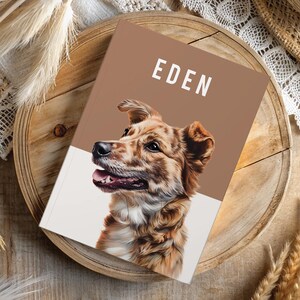 May include: A notebook with the name "EDEN" in white text on a brown background. The cover features a detailed illustration of a dog with brown and white fur. The notebook is on a wooden tray, surrounded by decorative elements.