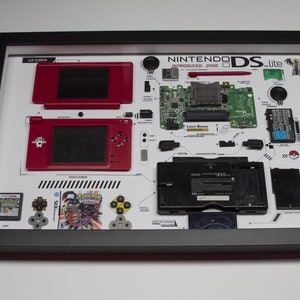 May include: A framed display of a disassembled Nintendo DS Lite, showing the individual components of the handheld gaming console. The display includes the top and bottom screens, the motherboard, the stylus, and the game cartridge slot. The console is red and black, and the display is on a white background.
