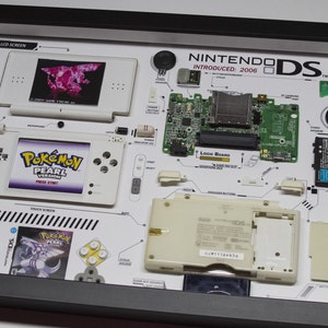 May include: A disassembled Nintendo DS Lite in a white frame with a white background. The frame includes the motherboard, screen, buttons, and other components. The frame also includes a Pokemon Pearl game cartridge and a Pokemon Pearl game case.