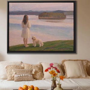 May include: A framed oil painting depicting a person with long hair wearing a light-colored dress standing on a grassy hill next to a small dog. They are looking out over a calm body of water toward a distant island under a soft, pastel-toned sky.
