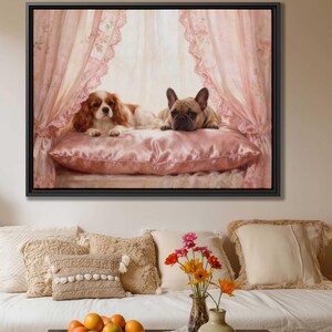May include: A framed print showing a Cavalier King Charles Spaniel and a French Bulldog lying on a pink satin pillow. The backdrop features pink curtains with lace detailing. The artwork is displayed above a sofa with decorative cushions and a vase of flowers.
