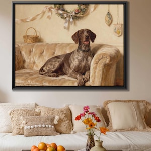 May include: A framed painting of a brown and white spotted dog resting on a beige tufted sofa. The dog is wearing a black collar and has its mouth open. A small wicker basket and floral wreath are visible in the background.