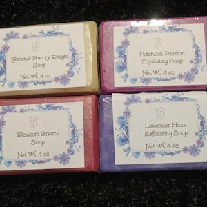 May include: Four wrapped soap bars with labels. The labels read "Almond Cherry Delight Soap", "Patchouli Passion Exfoliating Soap", "Blossom Breeze Soap", and "Lavender Haze Exfoliating Soap". Each bar is 4 oz.