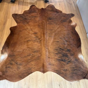 May include: A brown and black cowhide rug with a unique shape. The rug has a natural pattern with varying shades of brown and black. The rug is made of animal hide and is suitable for home decor.