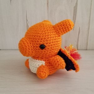 May include: Orange and white crocheted plush toy resembling a fire-type Pokemon with a black eye and a purple and orange tail.