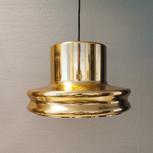 May include: A gold-coloured pendant light fixture with a round, layered design. The light fixture is hanging from a black cord.