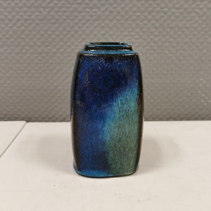 Peut inclure: Un petit vase en céramique de forme carrée avec un glaçage bleu et vert. Le vase a une base bleu foncé et un dessus bleu clair et vert.