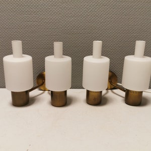 Könnte beinhalten: Vier Wandleuchten aus Messing mit weißen, mattierten Glasschirmen. Die Leuchten sind in einer Reihe miteinander verbunden.