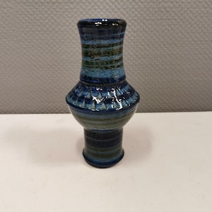 May include: A small blue and green ceramic vase with a striped pattern. The vase has a wide base and a narrow neck.