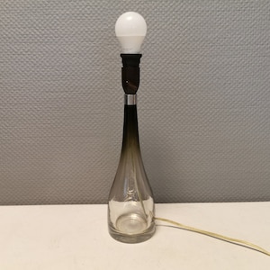 May include: A brown glass table lamp with a white light bulb. The lamp has a clear glass base and a silver metal accent.
