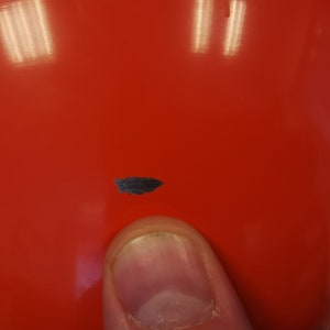 May include: A close-up of a bright red, round object with a small, dark grey mark on the surface.
