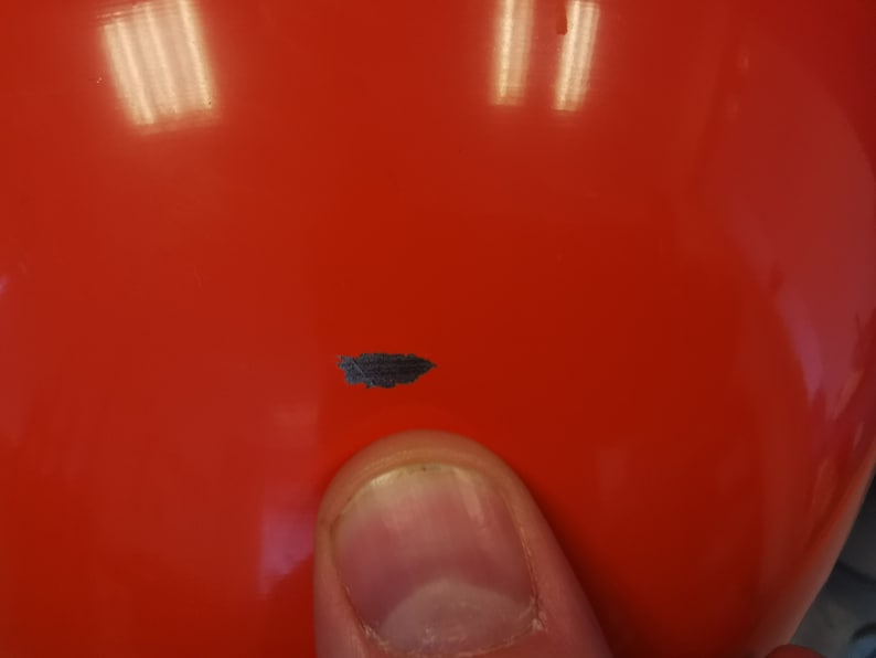 May include: A close-up of a bright red, round object with a small, dark grey mark on the surface.