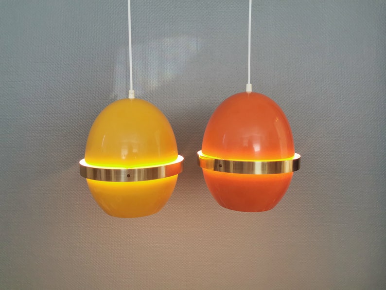 May include: Two hanging pendant lights with a gold metal band around the middle. The light on the left is yellow and the light on the right is orange.