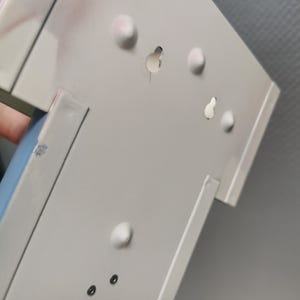 Puede incluir: Primer plano de un objeto met&aacute;lico blanco con varias protuberancias redondeadas y agujeros. El objeto tiene forma rectangular con un dise&ntilde;o ligeramente inclinado. La superficie muestra algo de decoloraci&oacute;n rosada.