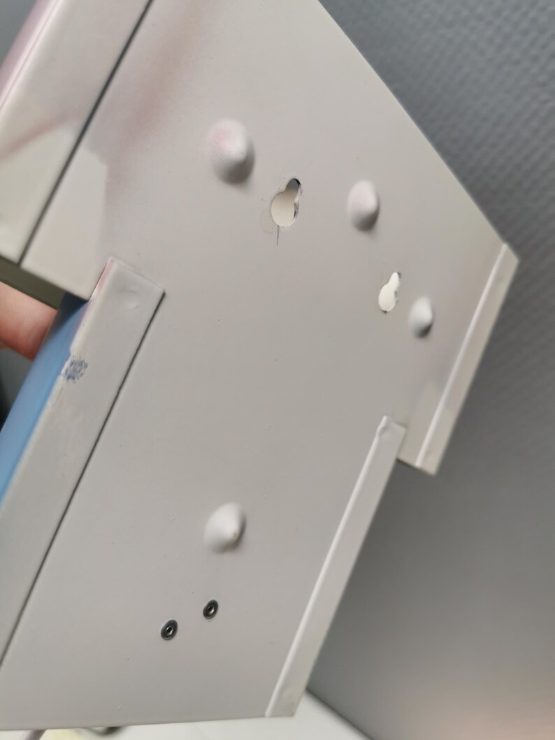 Puede incluir: Primer plano de un objeto met&aacute;lico blanco con varias protuberancias redondeadas y agujeros. El objeto tiene forma rectangular con un dise&ntilde;o ligeramente inclinado. La superficie muestra algo de decoloraci&oacute;n rosada.