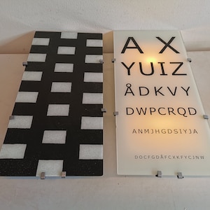 Puede incluir: Dos paneles de vidrio, uno con un patrón de cuadros en blanco y negro y el otro con una tabla de visión. La tabla de visión tiene las letras AX, YUIZ, ÅDKVY, DWPCRQD, ANMJHGDSIYJA, DOCFGDÅFCXKFYCJNW.