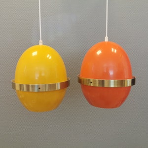 May include: Two egg-shaped pendant lights with brass trim. One light is yellow and the other is orange.