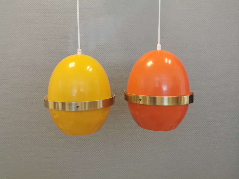 May include: Two egg-shaped pendant lights with brass trim. One light is yellow and the other is orange.