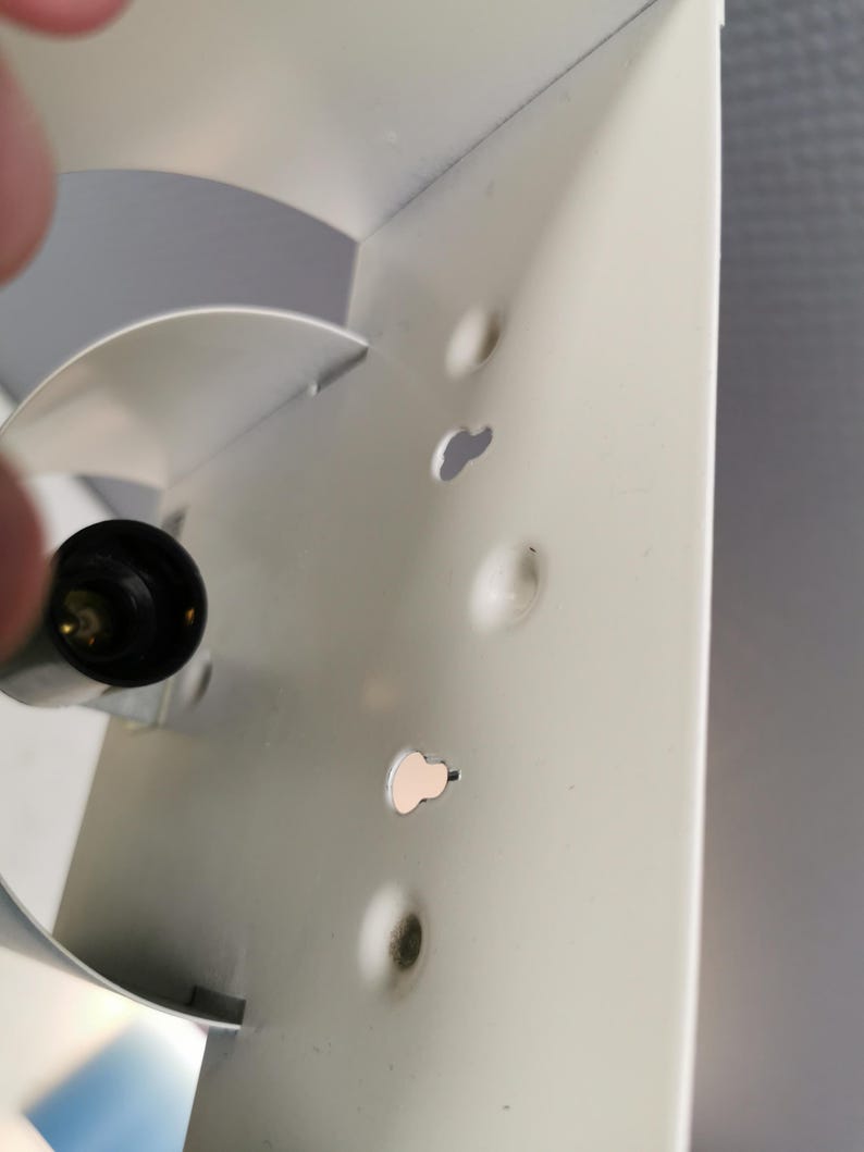 Puede incluir: Primer plano de una secci&oacute;n de un objeto met&aacute;lico blanco con varios agujeros peque&ntilde;os de forma irregular. Un objeto negro y redondeado con una punta dorada es visible en el lado izquierdo. El metal tiene algunas imperfecciones menores.