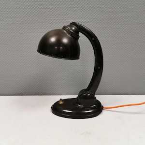 May include: A black desk lamp with a curved arm and a round, dark brown shade. The lamp has a black cord with an orange wire.
