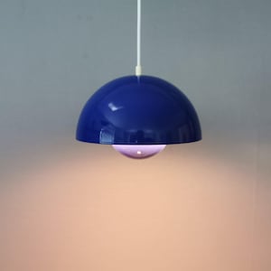 Könnte beinhalten: Eine glänzende, dunkelblaue, kuppelförmige Pendelleuchte, die an einem weißen Kabel hängt. Die Lampe verfügt über einen kleineren, halbkugelförmigen Schirm unter der Hauptkuppel, der ein warmes Licht aus der Mitte des Objekts ausstrahlt.