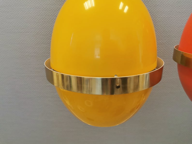 May include: Two hanging pendant lights with yellow and orange egg-shaped shades and gold metal rims.