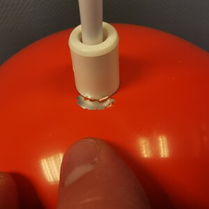 May include: Close-up of a red lampshade with a white cord and a silver metal ring around the top. The ring is slightly damaged.