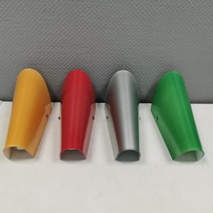 Puede incluir: Cuatro pantallas de lámpara de plástico en diferentes colores: amarillo, rojo, plateado y verde. Las pantallas de lámpara tienen todas la misma forma, con una parte superior curva y una parte inferior plana.