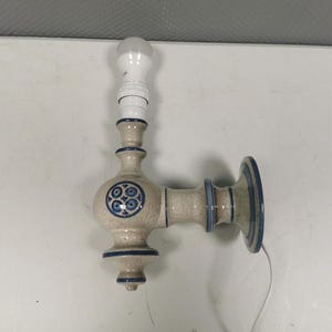 Puede incluir: Una lámpara de pared de cerámica con un diseño azul y blanco. La lámpara tiene una sola bombilla y un cable que cuelga.