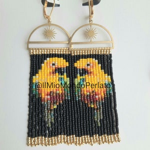 May include: Gold-toned metal earrings with a sunburst design and beaded fringe. The earrings feature a pixelated bird design in yellow, orange, and black beads. The text "@IlMioMondoPerlato" is visible.