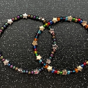 May include: Two star-shaped beaded bracelets. One bracelet has iridescent beads and the other has rainbow colored beads.