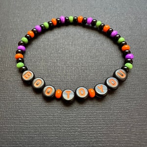 May include: A black beaded bracelet with orange and green beads spelling out "BOO TO YOU".