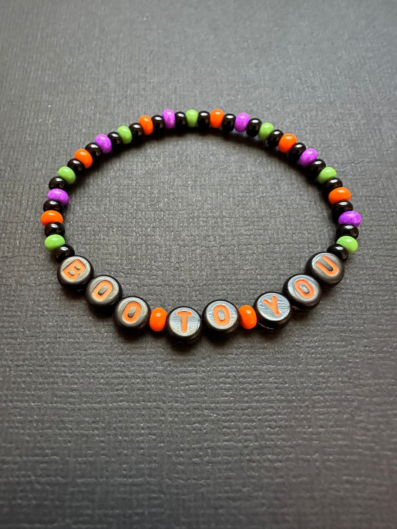 May include: A black beaded bracelet with orange and green beads spelling out "BOO TO YOU".