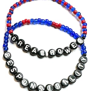 May include: Two beaded bracelets with the words "Great Power" and "Responsibility" spelled out in black beads with white lettering. The bracelets are made with blue and red beads.