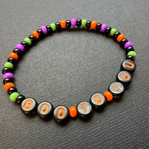 May include: A black beaded bracelet with orange, green, and purple beads. The bracelet spells out "BOO TO YOU" in orange letters.