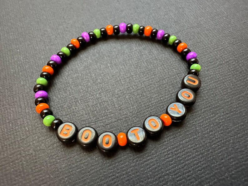 May include: A black beaded bracelet with orange, green, and purple beads. The bracelet spells out "BOO TO YOU" in orange letters.