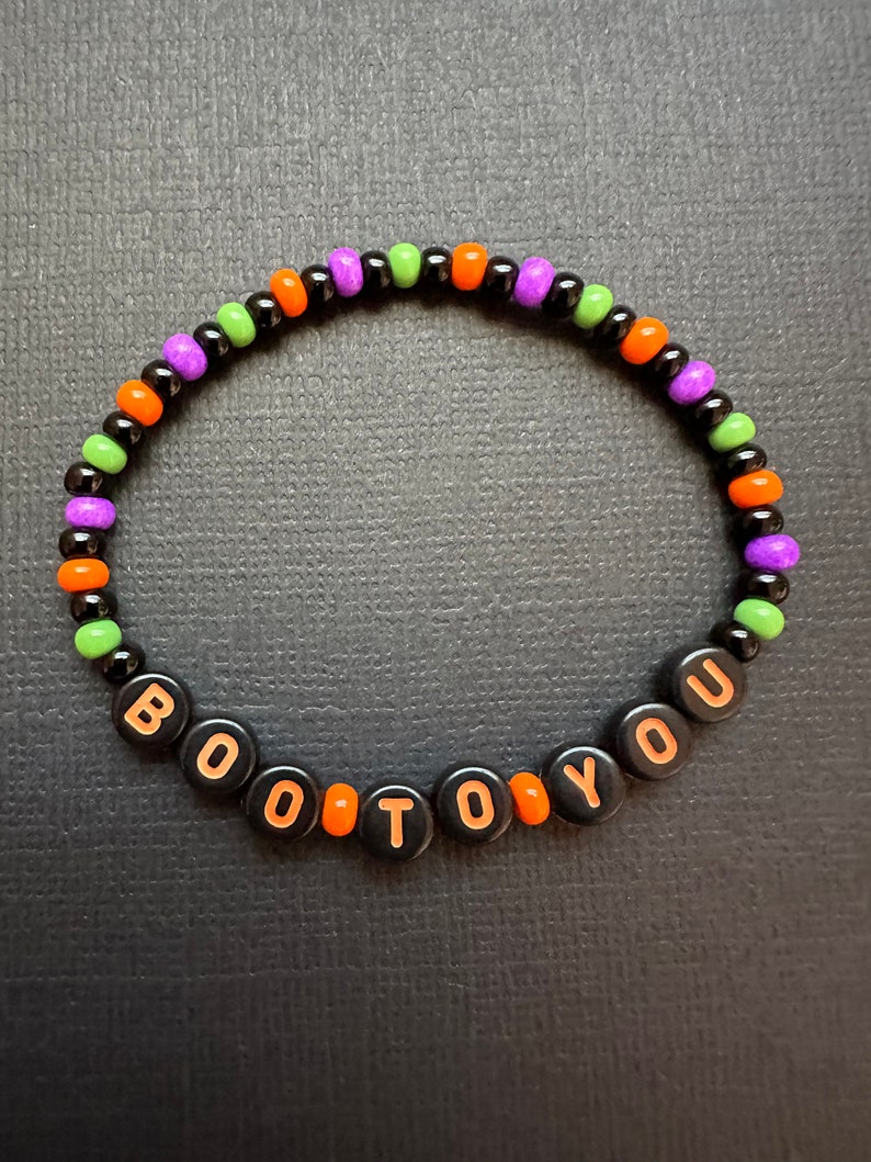 May include: A black beaded bracelet with orange, green, and purple beads. The bracelet spells out "BOO TO YOU" in orange letters.