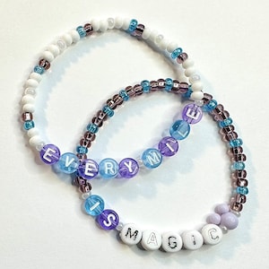 May include: Two beaded bracelets with the words "Every Mile Is Magic" spelled out in white and purple beads. The bracelets are made with white, purple, blue, and brown beads.