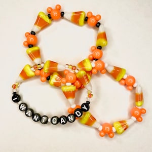 May include: Two candy corn bracelets with black beads spelling out "I WANT CANDY".