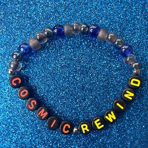 May include: A black beaded bracelet with the words "Cosmic Crew" in yellow and orange letters and "Wind" in yellow letters.