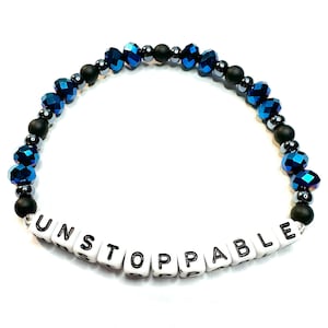 May include: A beaded bracelet featuring alternating dark blue faceted crystal beads, small metallic grey spacer beads, and matte black round beads. The center of the bracelet displays white square letter beads spelling out the word UNSTOPPABLE.