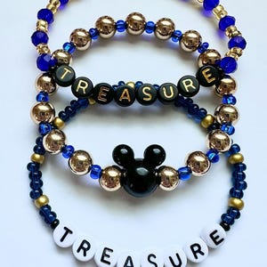May include: Four beaded bracelets in shades of blue and gold. One bracelet spells out "TREASURE" in white letter beads. Another features the word "TREASURE" in black letter beads. One bracelet has a black Mickey Mouse head charm.