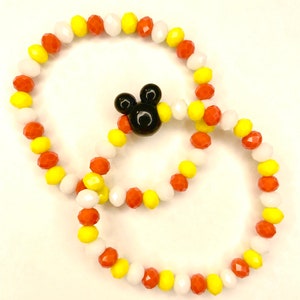May include: Two beaded bracelets with a Mickey Mouse charm. The bracelets are made with white, yellow, and orange beads.
