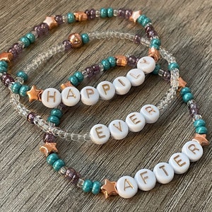 May include: Three beaded bracelets with gold stars and the words "Happily Ever After" spelled out in white beads.